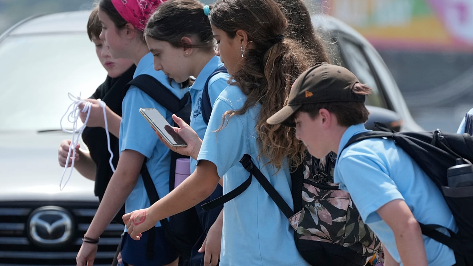 A school girl uses her phone as she walks with a group of kids in Sydney, Monday, Dec. 8, 2025.