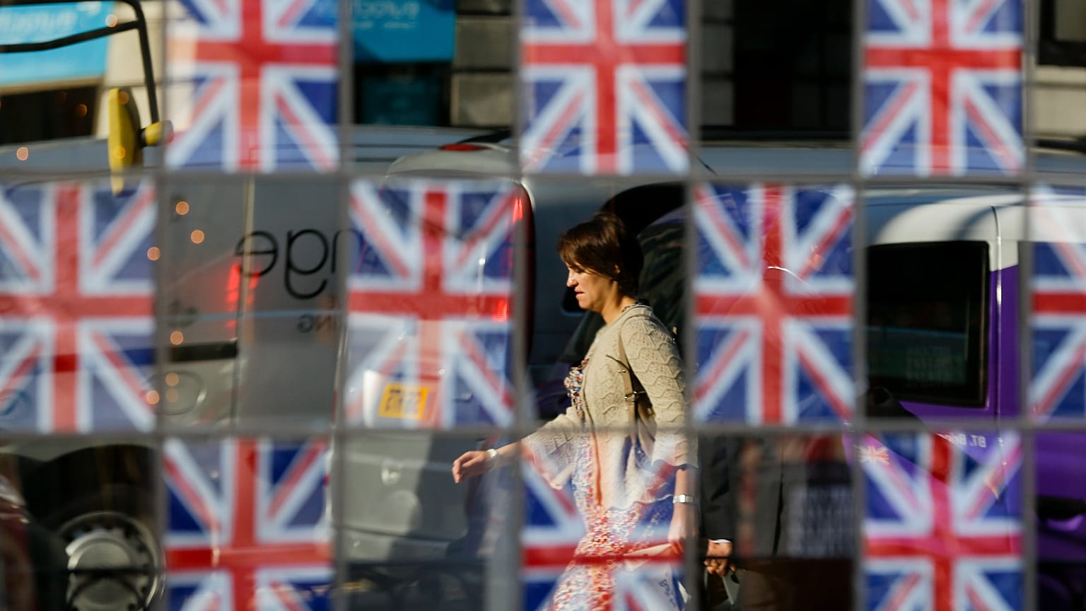 A commute is seen reflected in the glass of a pub window covered in British flags in London. 23 July 2012.