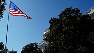 A large American flag is seen in front of the White House.