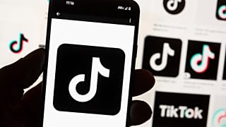 The TikTok logo is displayed n a mobile phone in front of a computer screen displaying the TikTok home screen, Oct. 14, 2022, in Boston