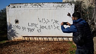 A Palestinian man takes a picture of a graffiti in Hebrew that was made during an Israeli settlers rampage.